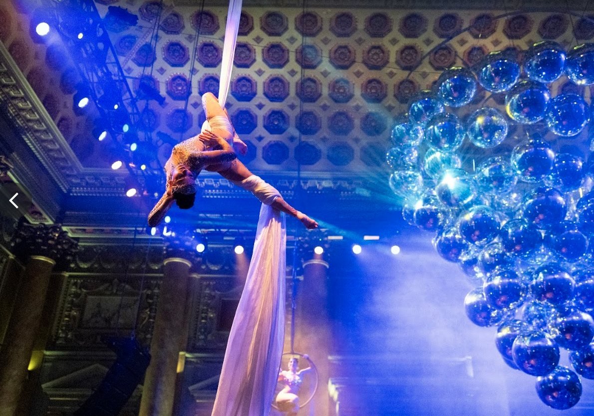 Aerial silk performers beside a cluster of mirrored disco balls in blue light