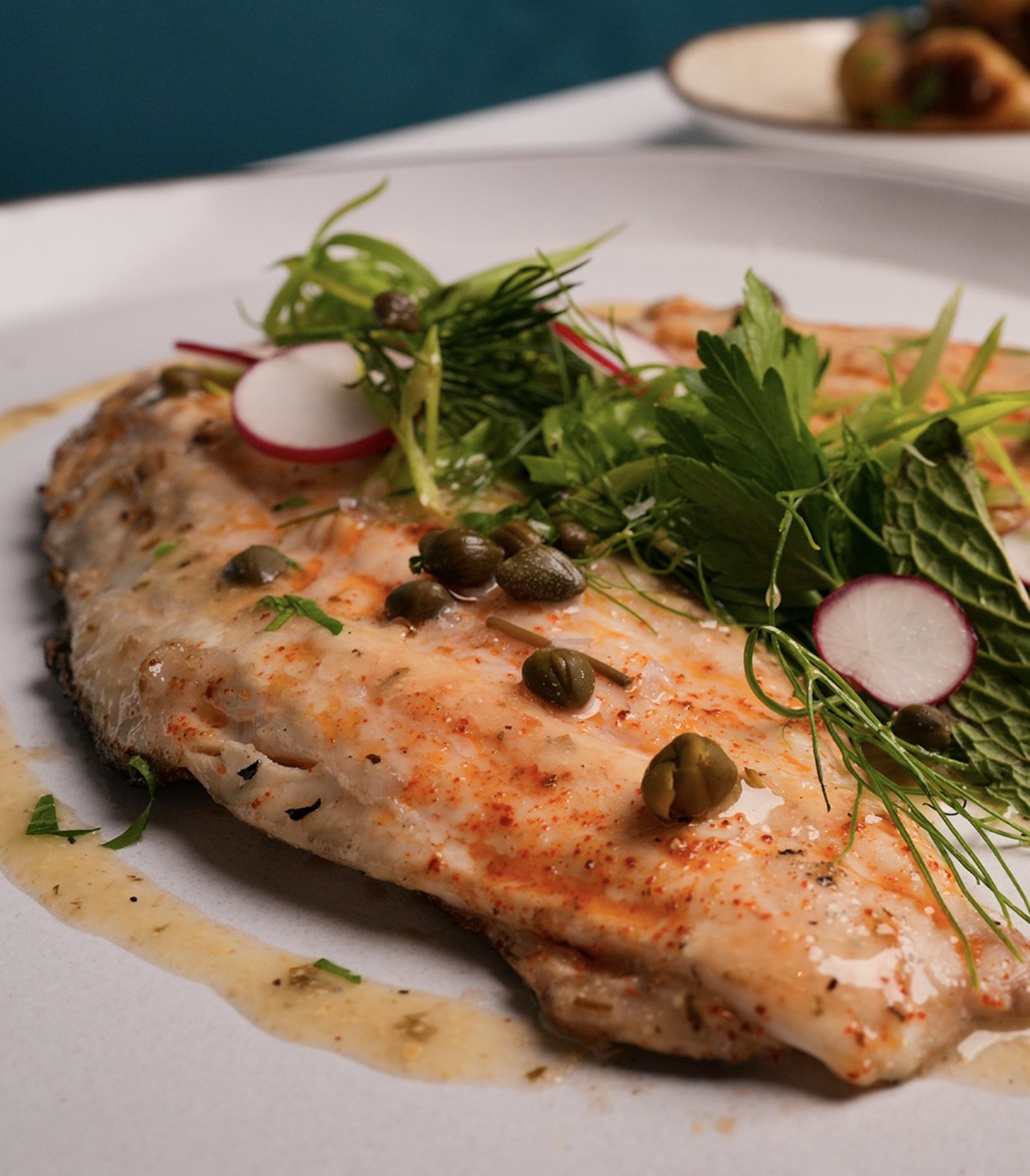 Grilled fish with capers, herbs and radish in a lemon butter sauce
